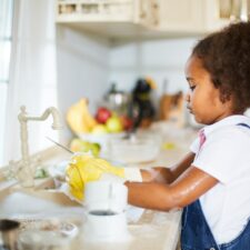 Little girl washing dishes in the kitchen learning life skills