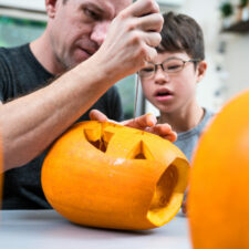 how to prepare child with special needs for halloween, iStock image of father and son with Downs Syndrome carving and preparing a pumpkin for Halloween