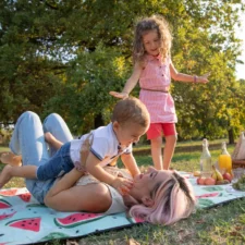family picnic at the park, iStock, Mother at a picnic plays with her children, lifts her son while her daughter watches, fruits and vegan food at the picnic.