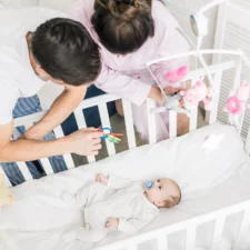 iStock image of mom and dad looking at their baby in a crib, article on safe sleep habits for infants