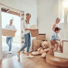 iStock image of parents with little kids moving into their new home. Excited couple carrying boxes up staircase with their son and daughter. Adorable children helping to unpack and move into property