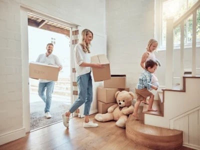 iStock image of parents with little kids moving into their new home. Excited couple carrying boxes up staircase with their son and daughter. Adorable children helping to unpack and move into property