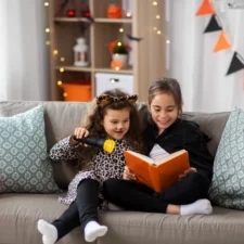 iStock image of Girls in halloween costumes reading book at home, The Best Halloween Books for Kids: by Age Group