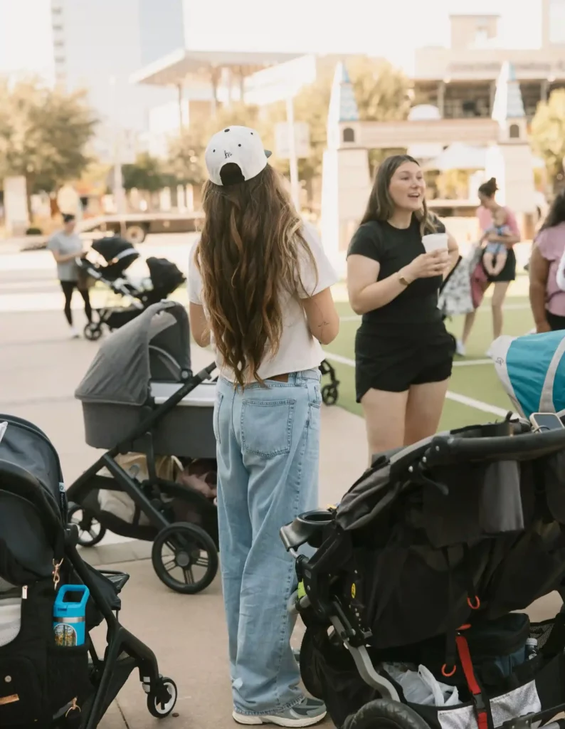 Image of women talking and drinking coffee, with their young children in strollers, at an event with The Mom Walk Collective groups in Dallas-Fort Worth, photo courtesy @honeylandphoto via Instagram