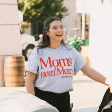 Image of a woman wearing a shirt that reads "Moms need moms" for an event with The Mom Walk Collective groups in Dallas-Fort Worth, photo courtesy @honeylandphoto