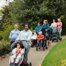 iStock image of a group of moms all walking together with their young children in strollers, for an article on The Mom Walk Collective groups in Dallas-Fort Worth