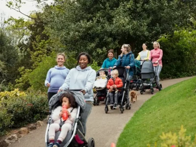 iStock image of a group of moms all walking together with their young children in strollers, for an article on The Mom Walk Collective groups in Dallas-Fort Worth