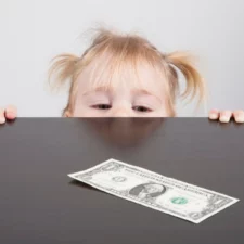 iStock image of little girl looking over the table edge at a dollar bill, for advice column on how parents ought to react, according to a Plano counselor, when they catch their child stealing