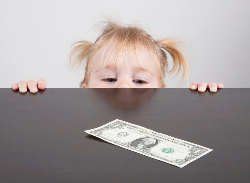iStock image of little girl looking over the table edge at a dollar bill, for advice column on how parents ought to react, according to a Plano counselor, when they catch their child stealing