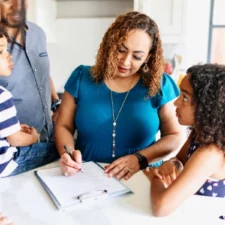 iStock image of mother reading and signing a form, surrounded by her children