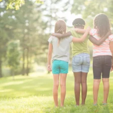 A multi-ethnic group of elementary age girls are standing together in a row with their arms around each other