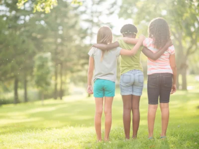 A multi-ethnic group of elementary age girls are standing together in a row with their arms around each other
