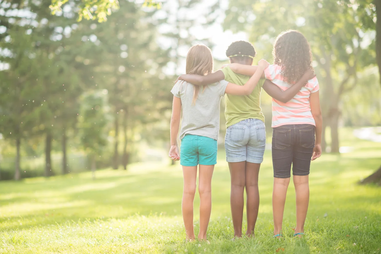 A multi-ethnic group of elementary age girls are standing together in a row with their arms around each other